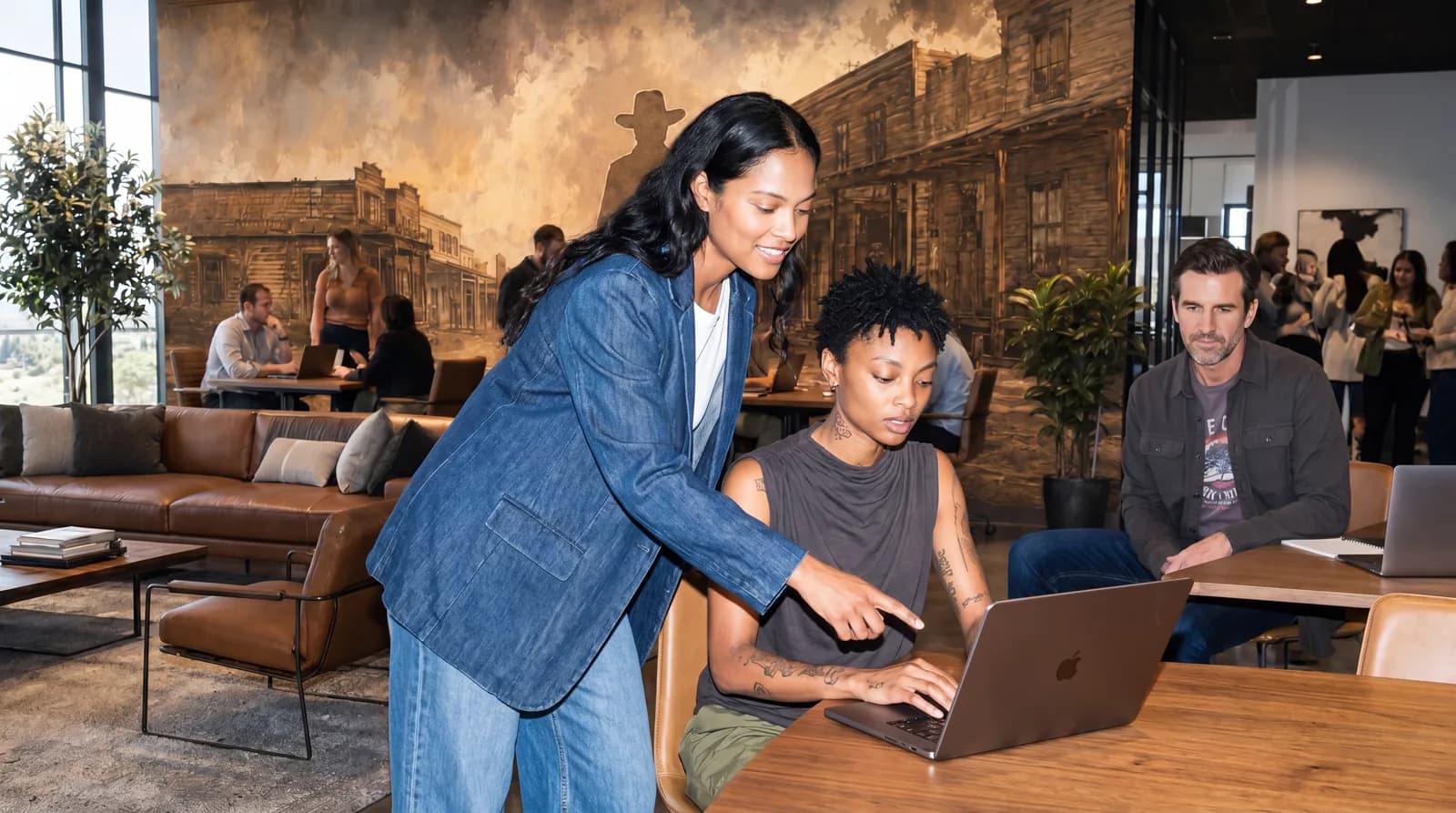 Two people review a laptop in a lounge with a large wall mural.