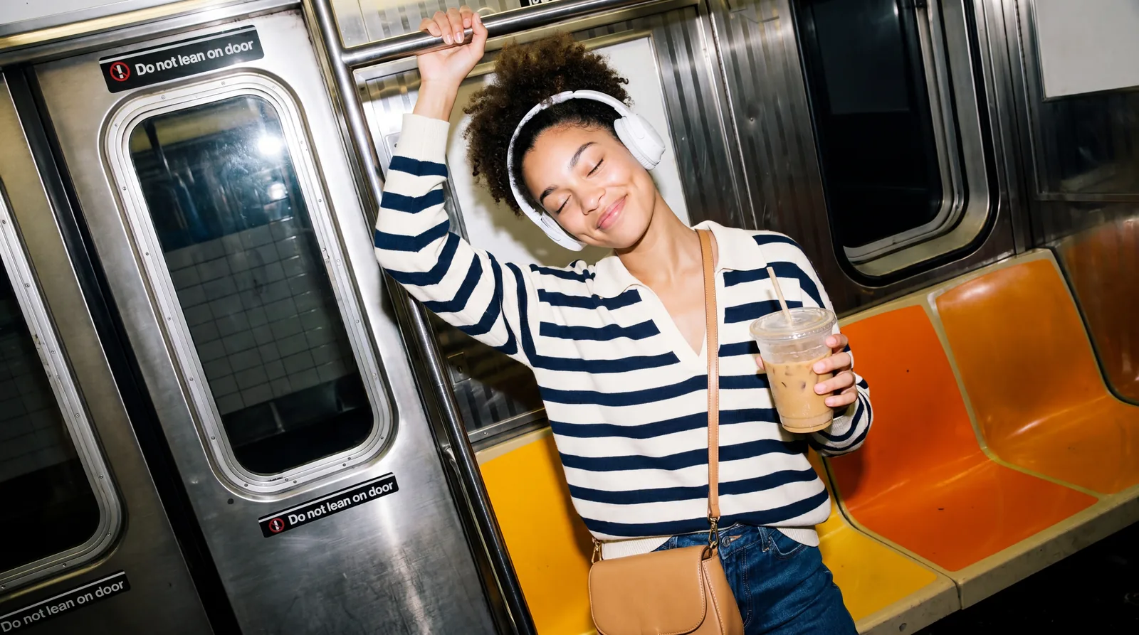 A person holding a drink rides a subway train.