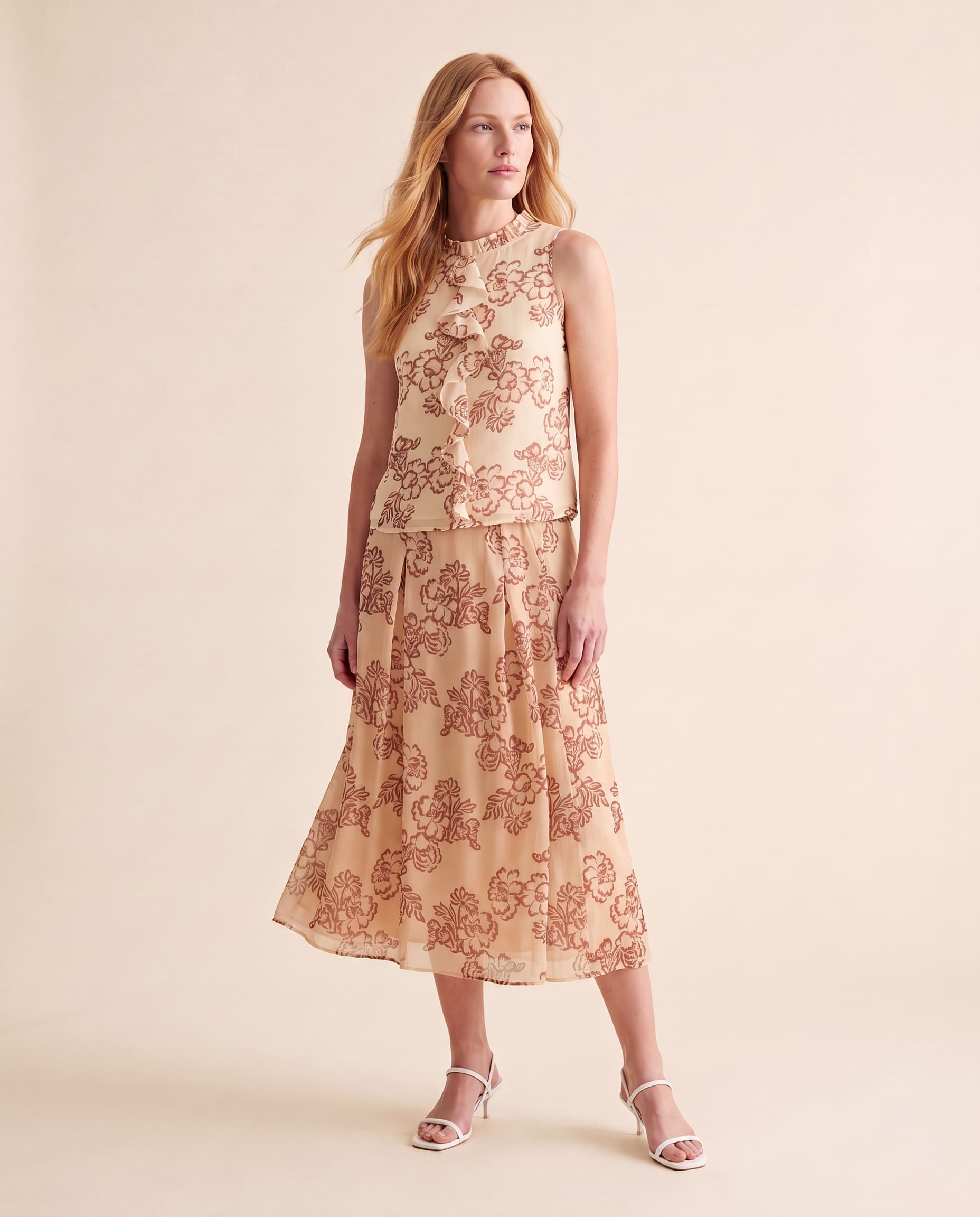 An AI model wears the Cartolina Bea skirt and Cassie ruffle top, both in the peony floral print, standing full length on a cream studio backdrop.