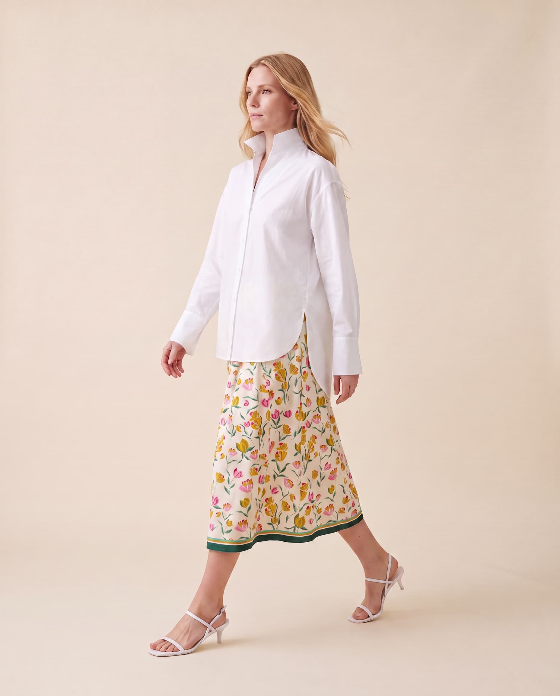 An AI model walks in the Cartolina Betsey shirt in white, worn untucked with its long curved back tail over the Kylie tiered skirt in the boho print.