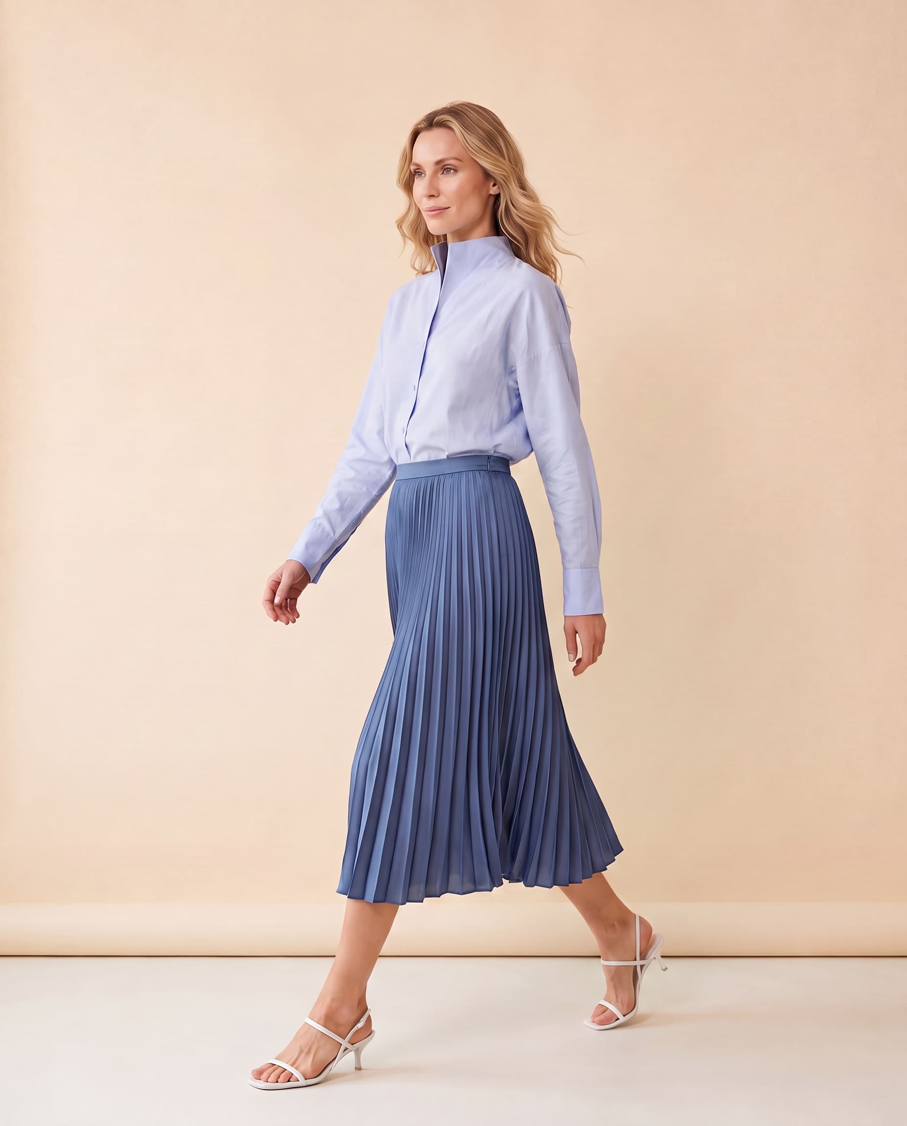 An AI model wears the Cartolina Betsey chambray shirt tucked into the Claudia pleated skirt in gallery blue, standing full length on a cream studio backdrop.