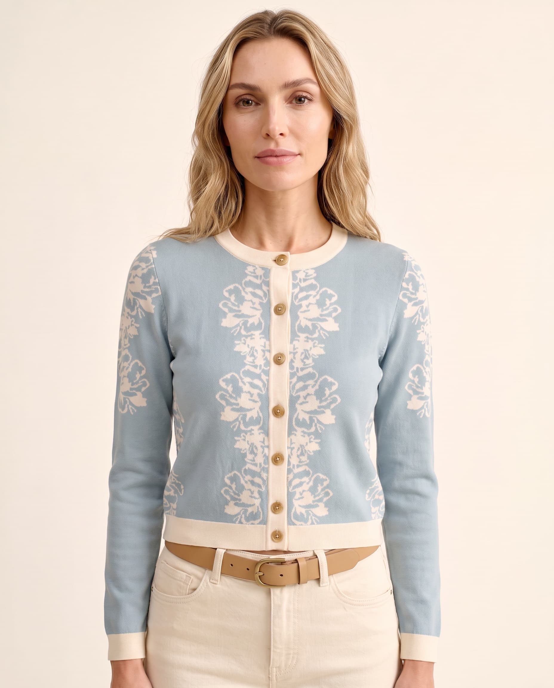 An AI model wears the Cartolina Fleur cardigan in stone blue with an ivory floral jacquard, buttoned over white jeans in a close crop.