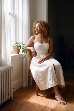 Campaign image: the model sits by an apartment window in morning light.