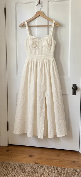 A phone photo of an ivory cotton sundress on a hanger, hung on a bedroom door.