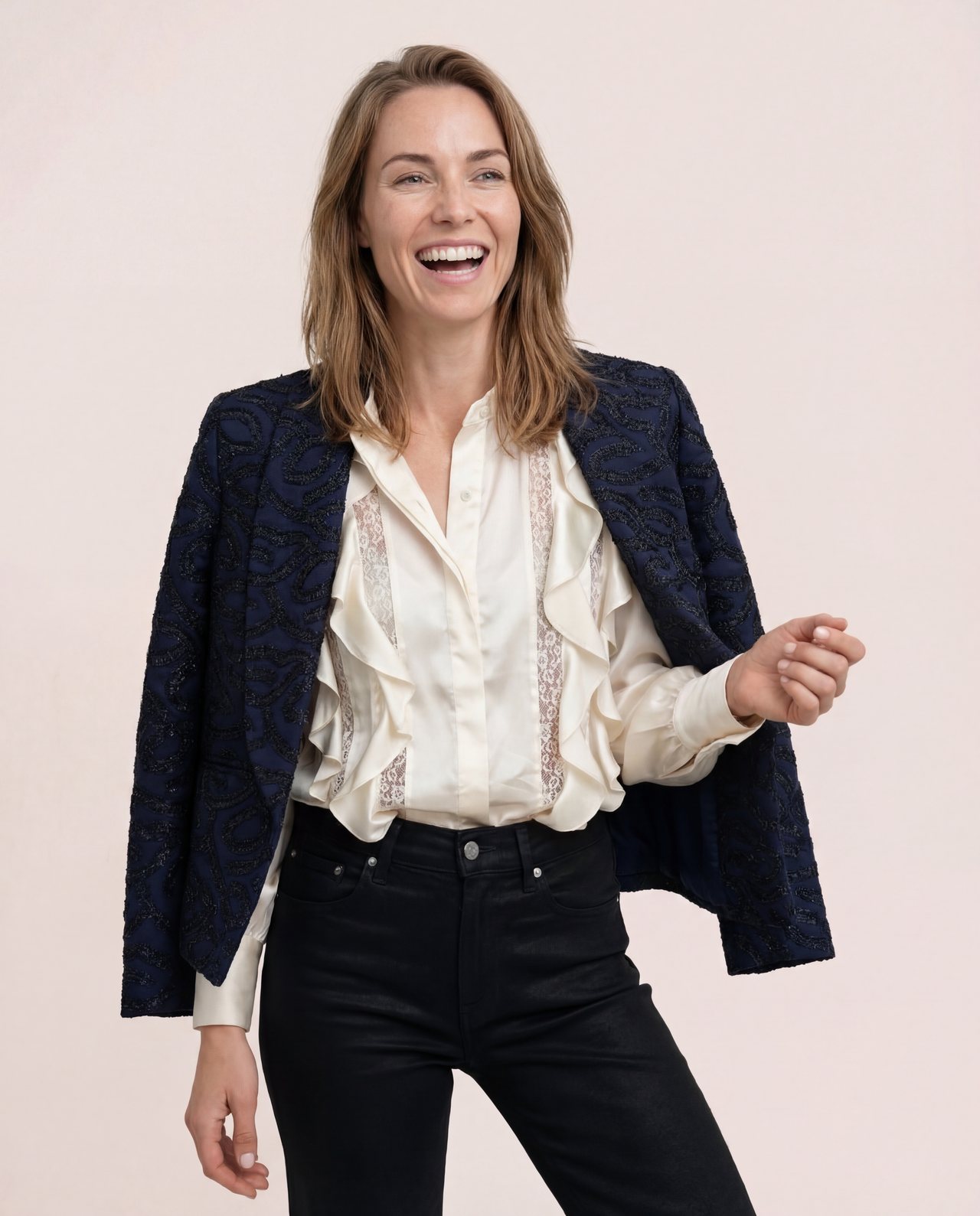 An AI model laughs in the Cartolina Anywhere jacket in Twilight Magic over the ivory Izzy top and black jeans, on a blush studio backdrop.