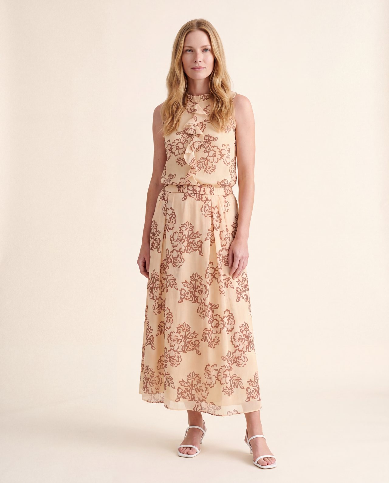 An AI model wears the Cartolina Bea skirt and Cassie ruffle top, both in the peony floral print, standing full length on a cream studio backdrop.