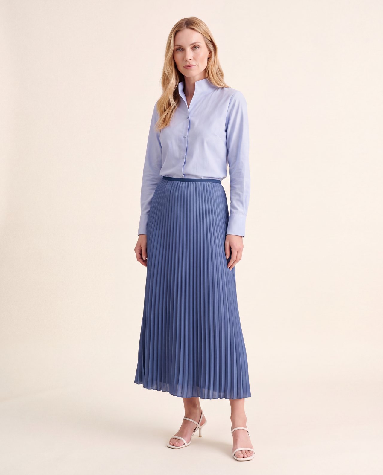 An AI model wears the Cartolina Betsey chambray shirt tucked into the Claudia pleated skirt in gallery blue, standing full length on a cream studio backdrop.