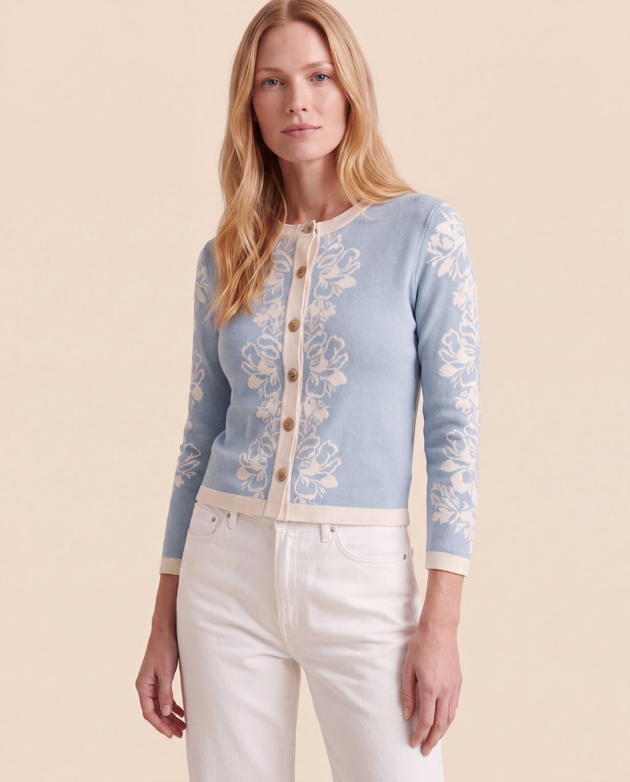 An AI model wears the Cartolina Fleur cardigan in stone blue with an ivory floral jacquard, buttoned over white jeans in a close crop.