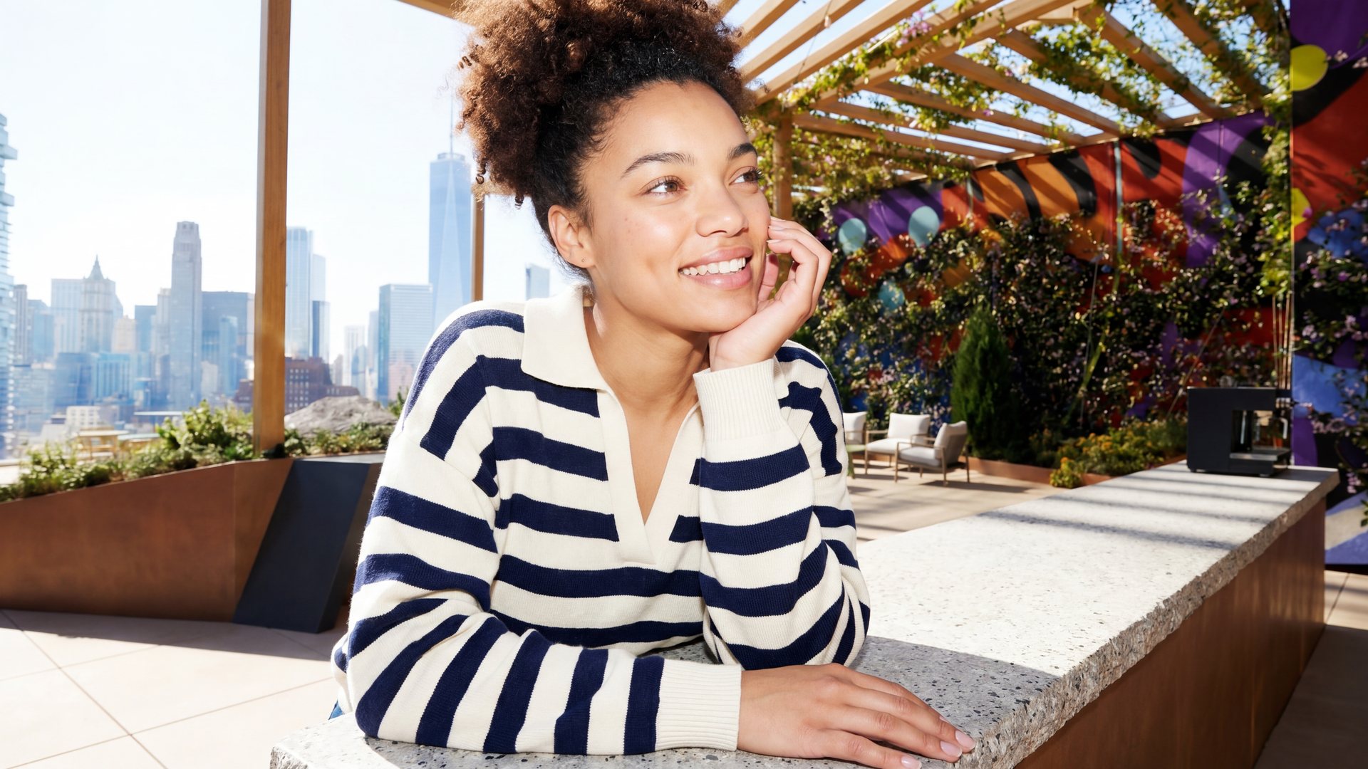 A woman in a striped sweater rests her chin on her hand on a One Grand terrace above the lower Manhattan skyline.